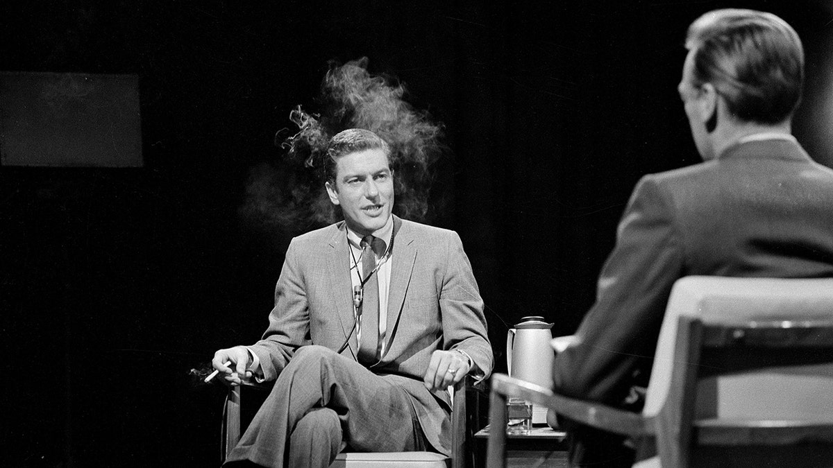 Dick Van Dyke on stage in conversation while smoking a cigarette.