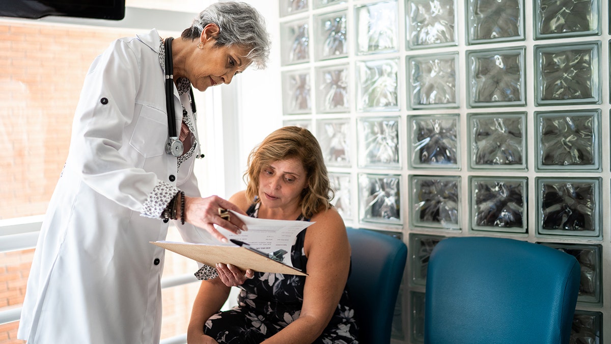 Doctor reviewing medical paperwork with a patient in a clinic waiting area.