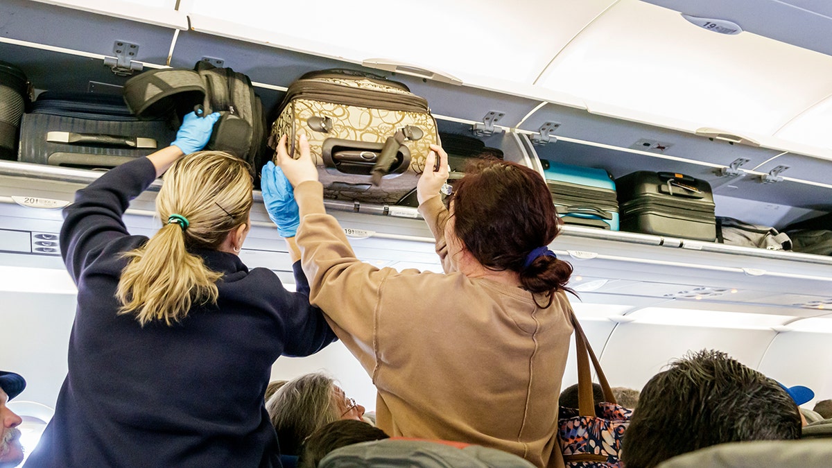Passengers placing carry-on luggage into the crowded overhead bins of a commercial airplane cabin.