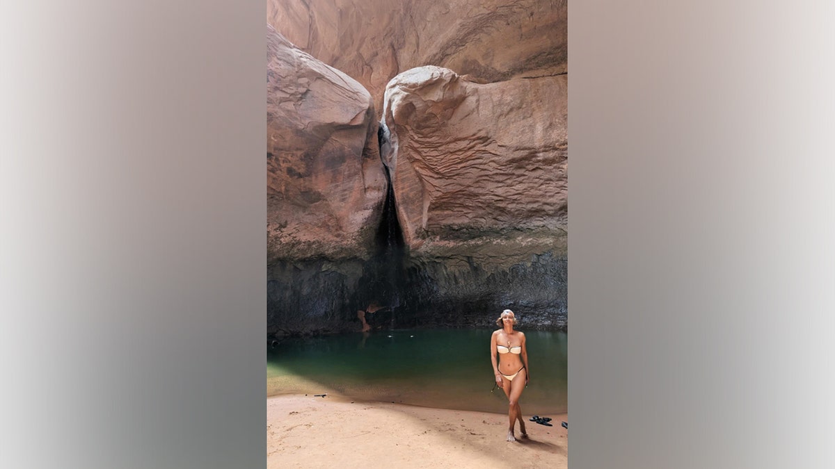 Halle Berry poses on a sandy shoreline at Lake Powell wearing a light-colored bikini, with canyon walls and a waterfall visible in the background in her July 29, 2025, Instagram photo.