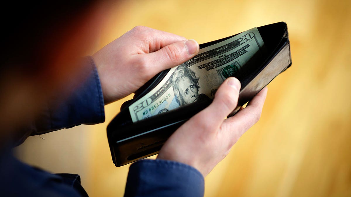 An image of a man's hand holding an open wallet with dollar bills inside.