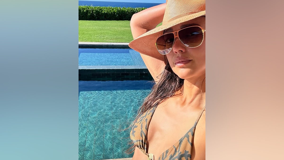 Jessica Alba poses for a poolside selfie while wearing sunglasses and a hat.