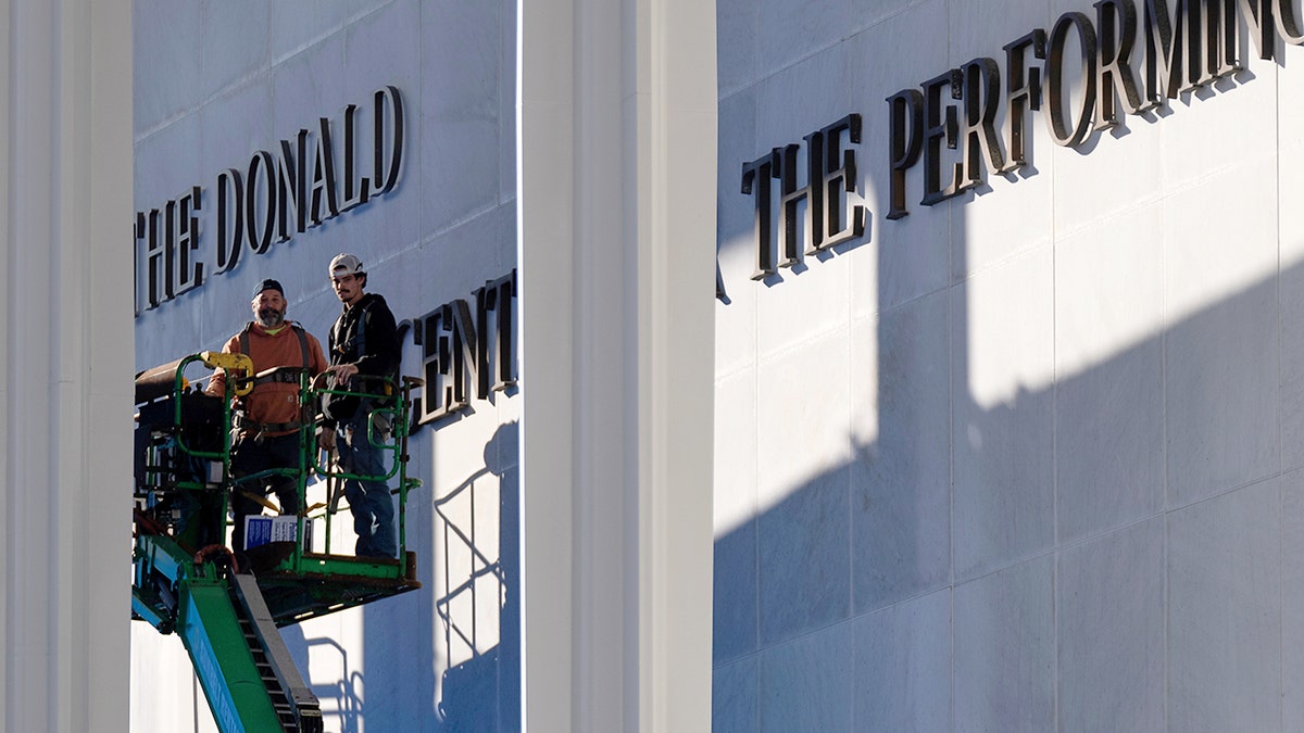 Two workers stand on a forklift near 