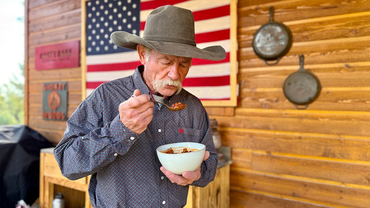 A cowboy eats a bowl of chili with a spoon.