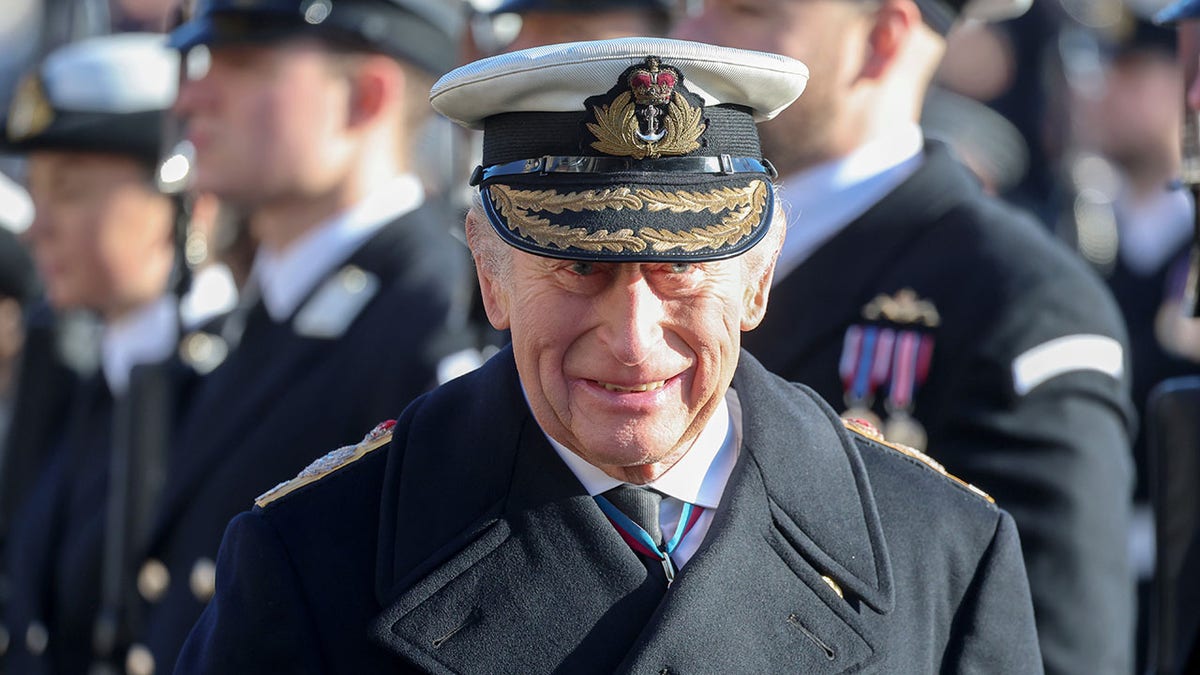 King Charles smiling in a dark military suit.