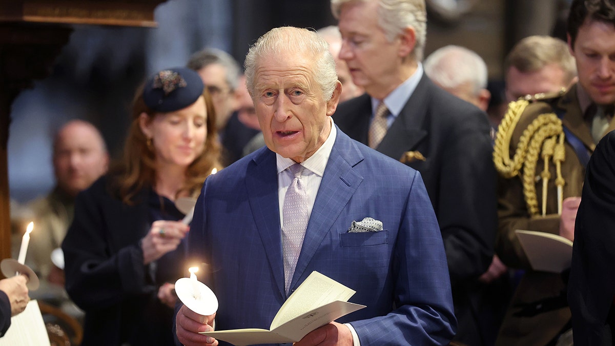 King Charles singing a hymn while holding a lit candle.