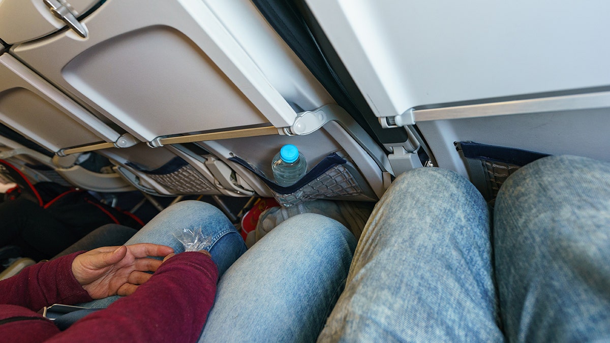 Limited legroom in economy class airplane seating with passenger knees close to the seatback.