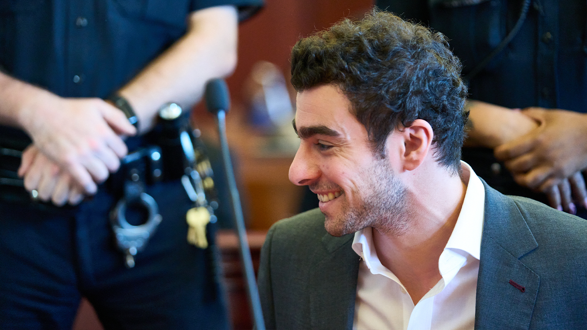 Luigi Mangione smiles in court while looking to the left.