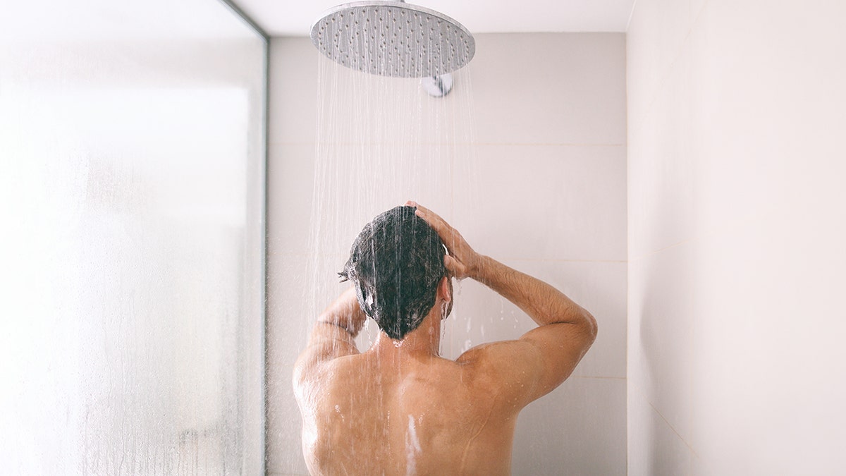 Person showering under a rainfall showerhead, washing their hair in a modern bathroom.