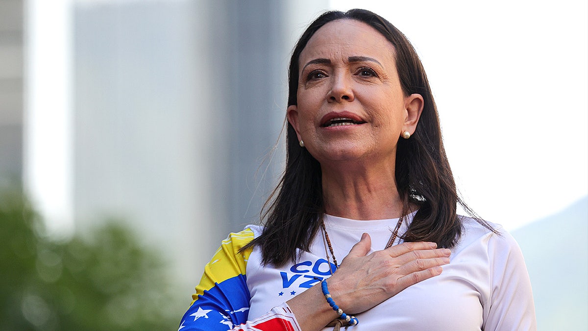 Venezuelan opposition leader María Corina Machado stands with her hand over her heart.