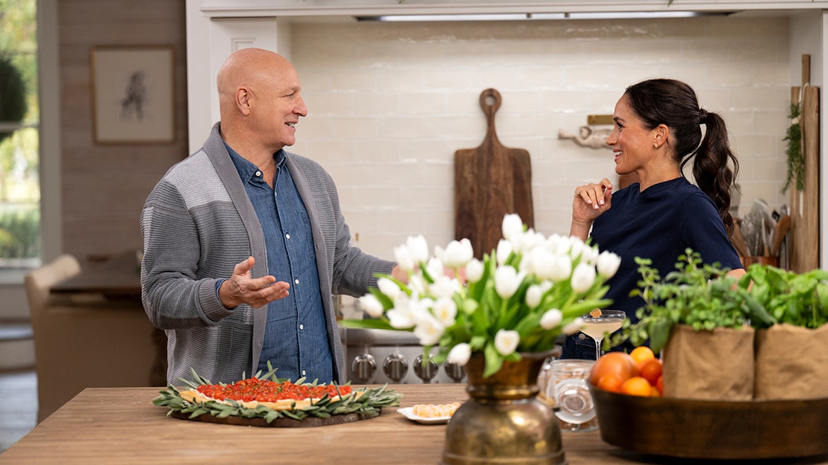Meghan Markle speaking to a laughing Tom Colicchio inside a well-decorated Montecito home.