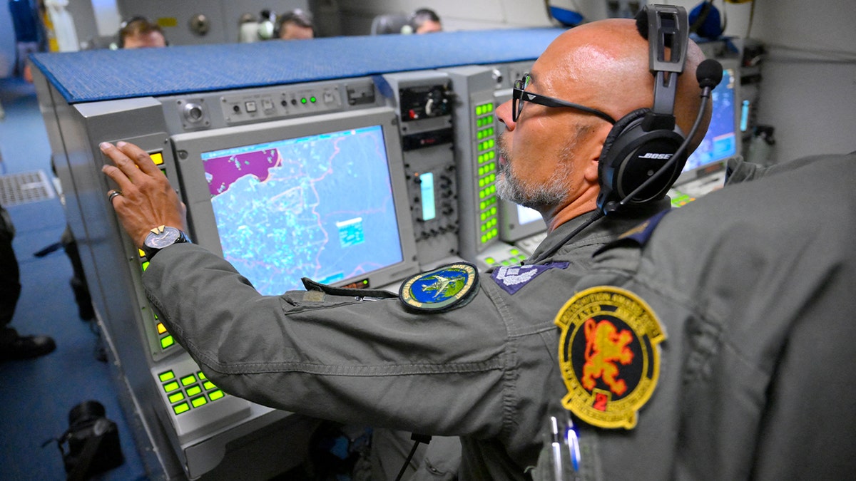 A military officer monitors radar and sensor displays inside an airborne command aircraft during a surveillance flight.