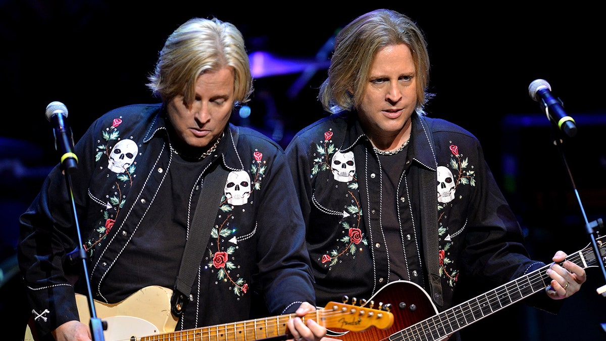 Los gemelos Nelson, con chaquetas vaqueras de inspiración rockabilly, tocando la guitarra en el escenario.