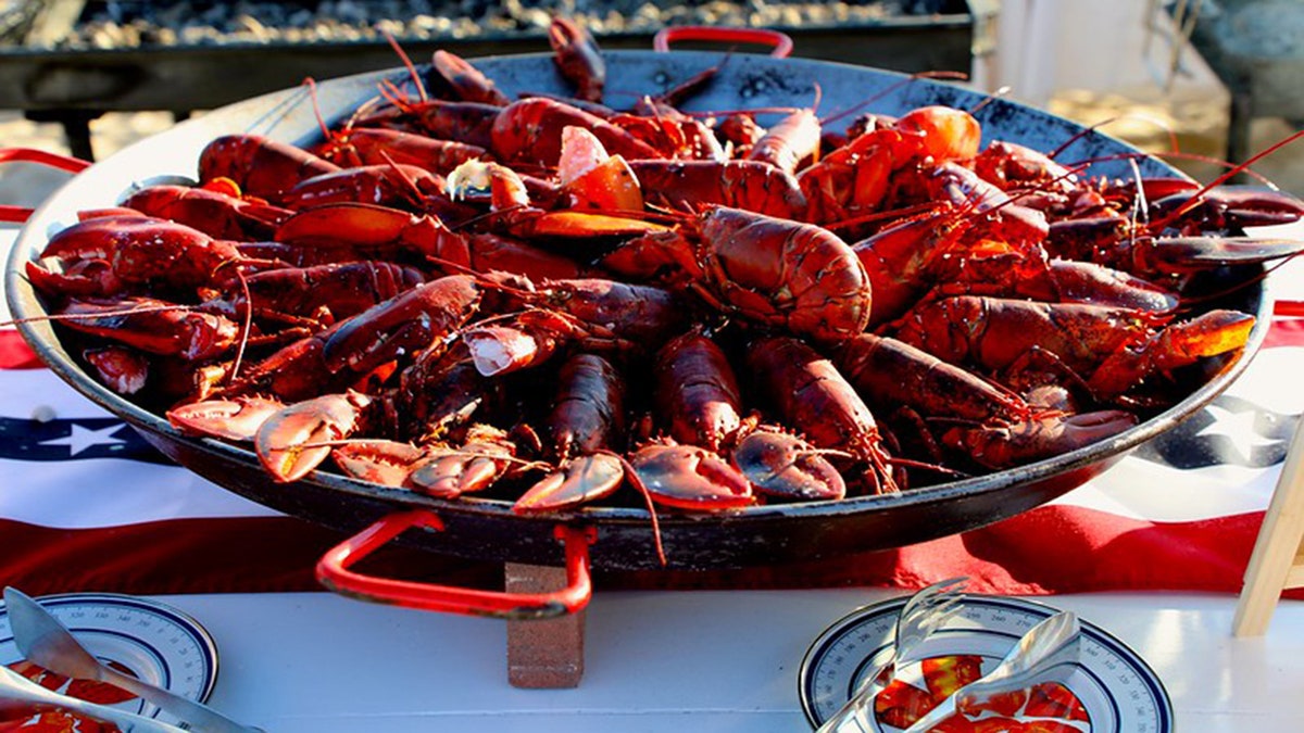 桌子上擺著一個大盤子，裡面裝滿了煮熟的龍蝦，還有餐具。