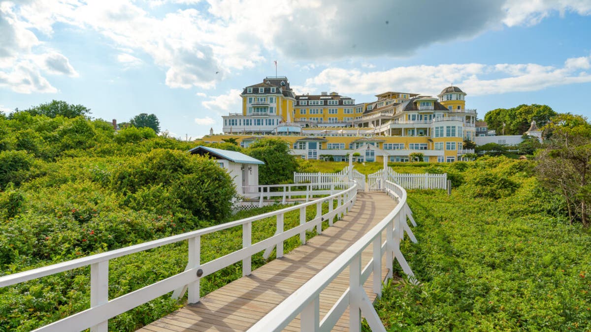 帶有白色欄杆的彎曲木板路穿過綠色灌木叢，通向黃白色的海洋之家酒店。