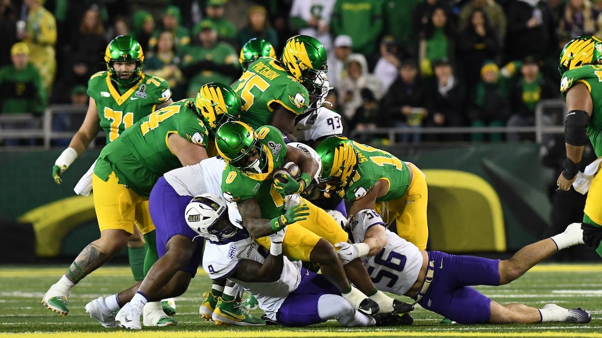 Oregon Ducks running back Jordon Davison (0) runs the ball against James Madison Dukes defensive end Xavier Holmes (9) and linebacker Drew Spinogatti (56) during the College Football Playoff first round game between the Oregon Ducks and James Madison Dukes on December 20, 2025 at Autzen Stadium in Oregon.