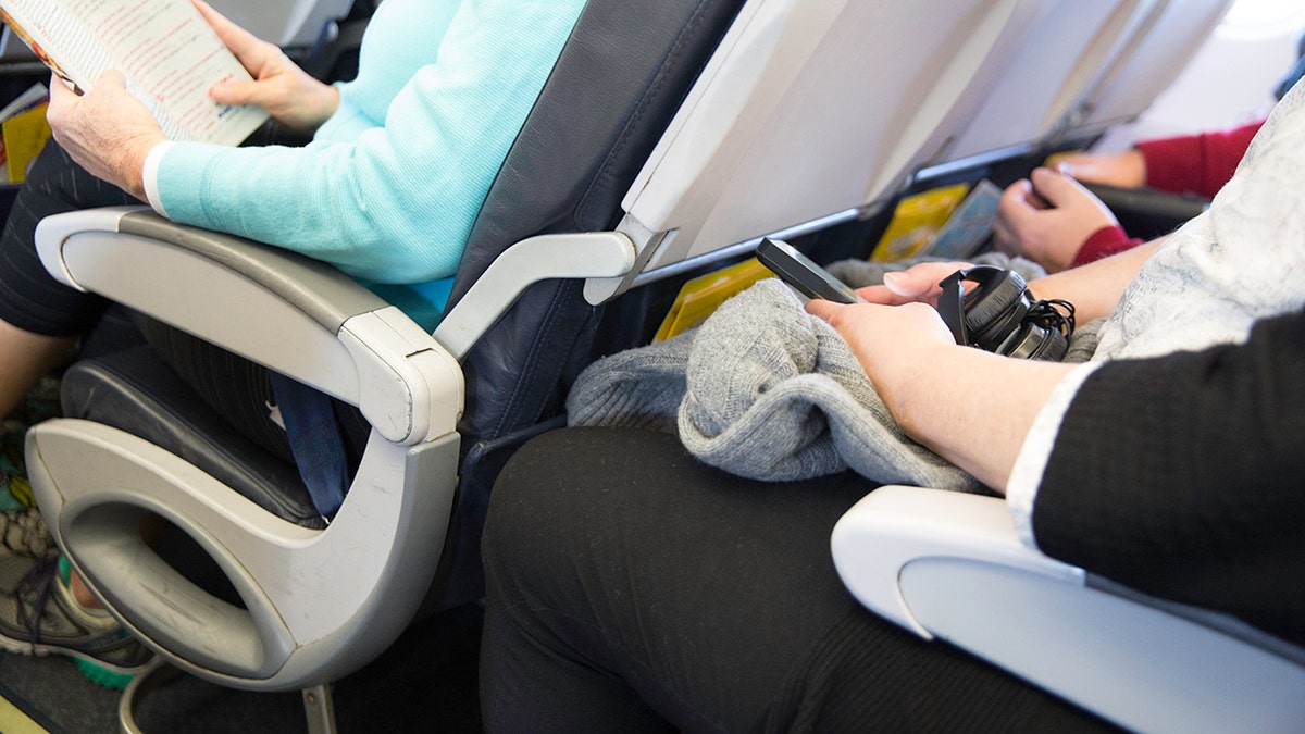 Passengers seated closely together in economy class airplane seats during a commercial flight.