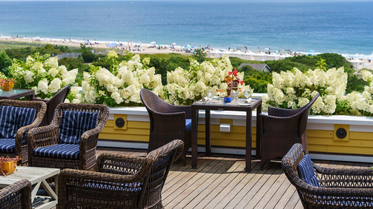 位於 Watch Hill 的 Ocean House 的戶外露台設有柳條座椅、盛開的白色繡球花，以及以繁華海灘為背景的海景。