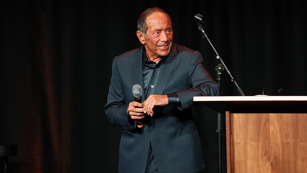 Paul Anka on stage holding a mic and looking away.