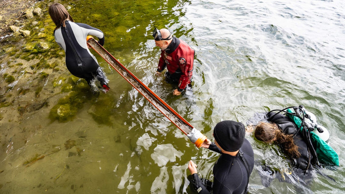 Archaeologists taking spear out of water