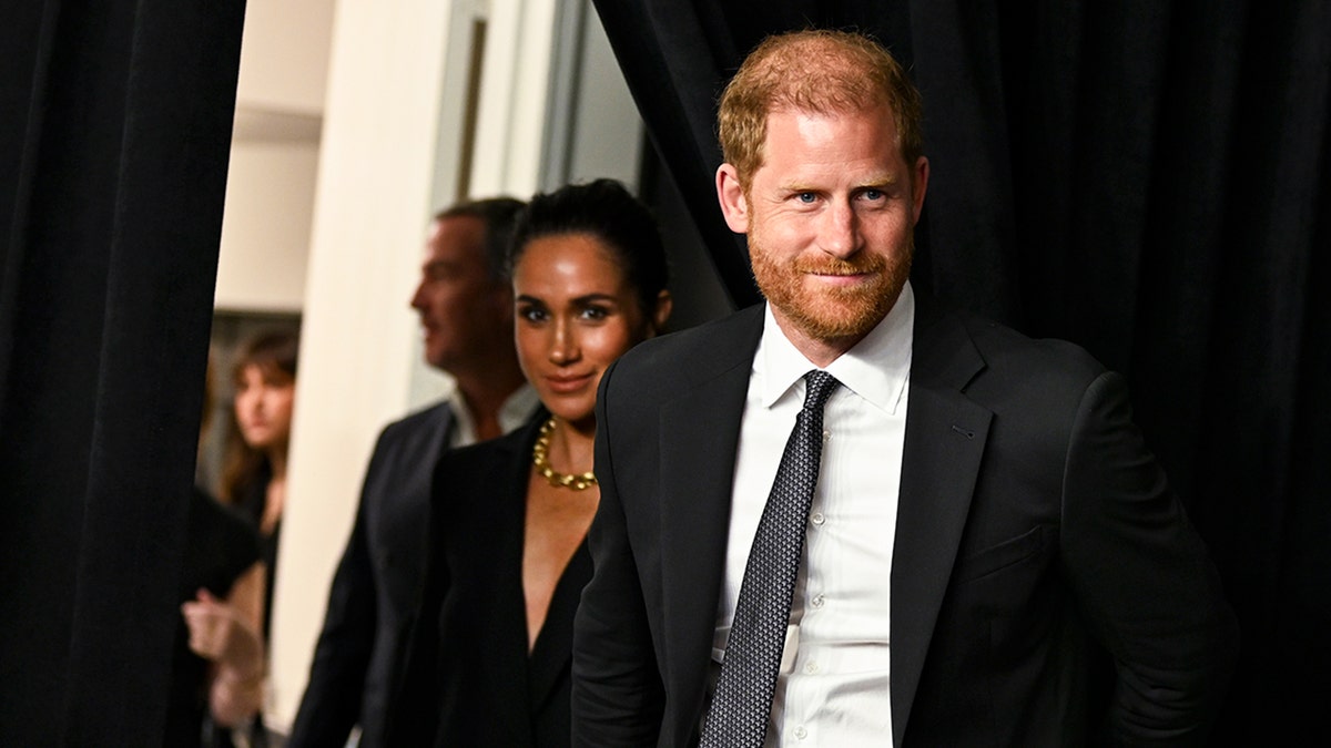 Prince Harry walking in front of Meghan Markle as they wear matching dark suits.