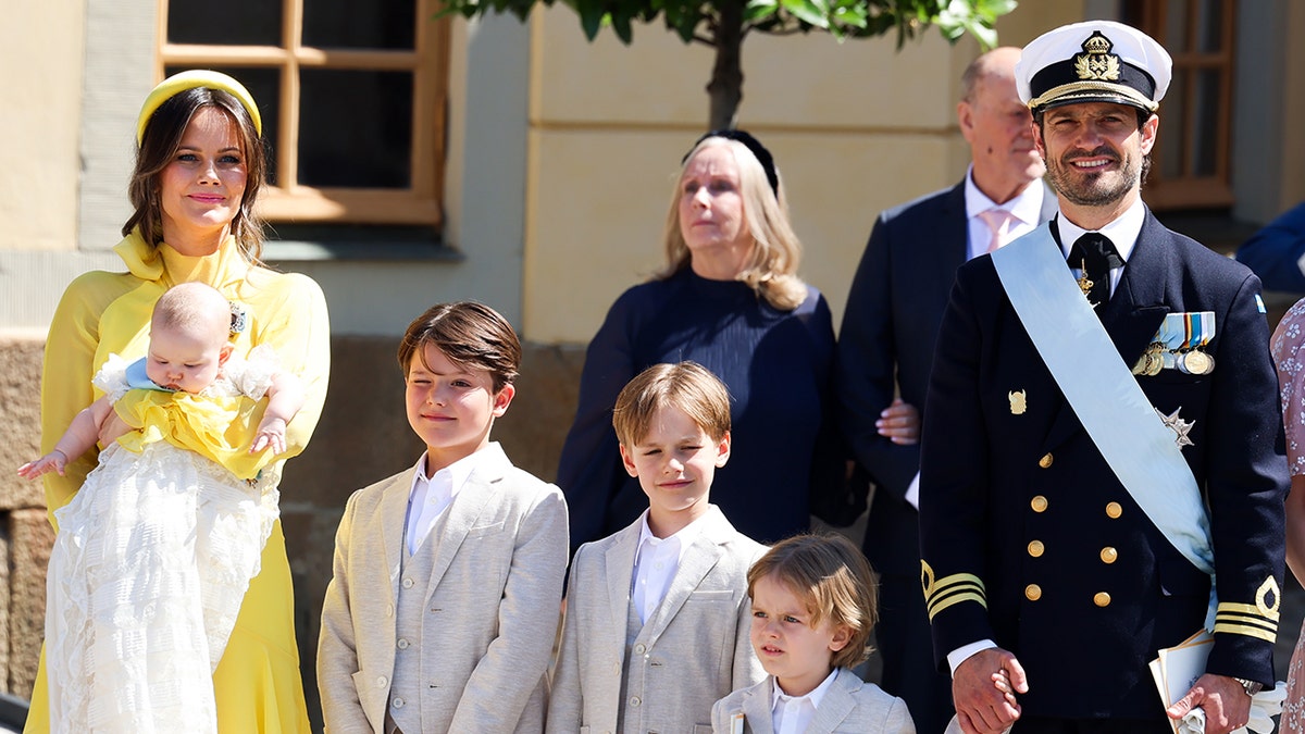 Princess Sofia holding her baby wearing a yellow dress next to her three other children and her husband Prince Carl Philip.