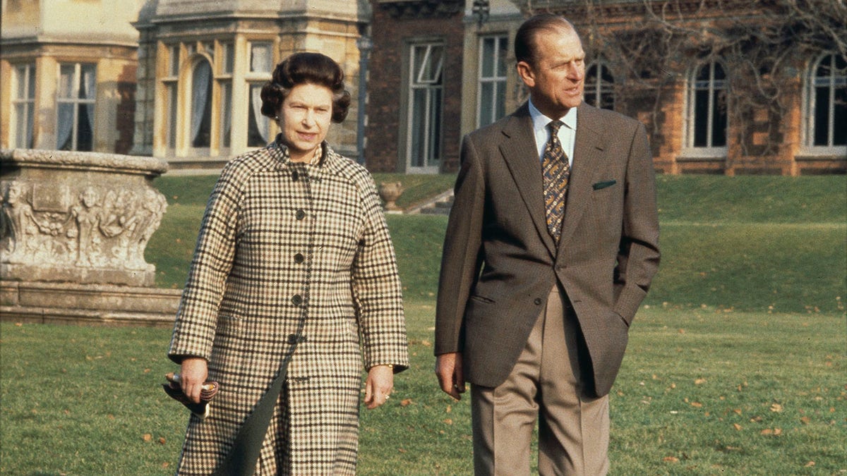 Queen Elizabeth II and Prince Philip watching together in matching brown attire outside of Sandringham.