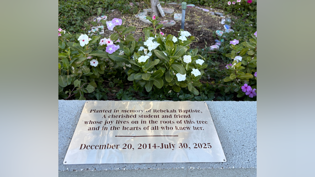 A memorial plaque honoring Rebecca Baptiste sits in front of flowering plants