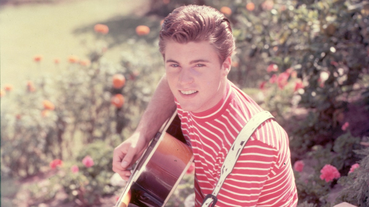 A young Ricky Nelson wearing a red and white striped shirt playing guitar.