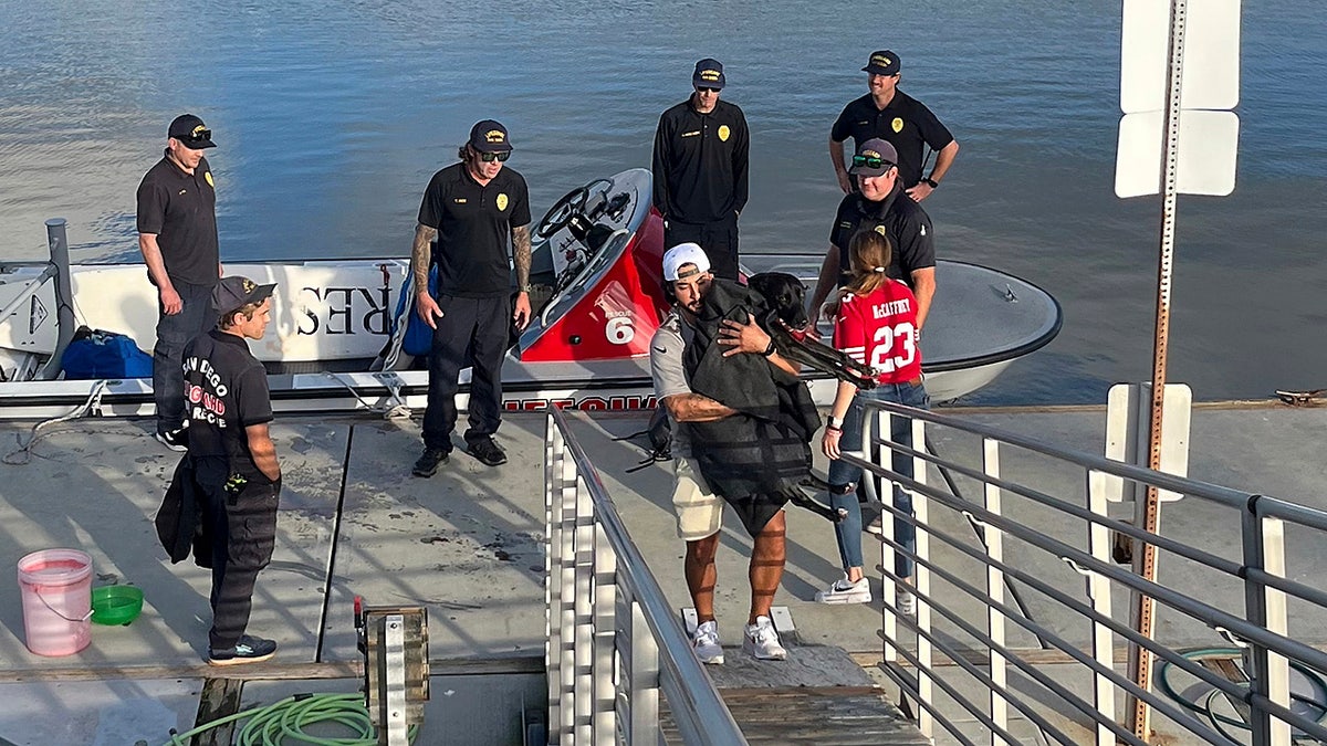 This photo released by San Diego Fire-Rescue shows Sadie, a black Labrador retriever-mix, being picked up by her parents Brandon and Alexis after Sadie was rescued from the water near Mission Beach, San Diego, Nov. 23, 2025. (San Diego Fire-Rescue via AP)