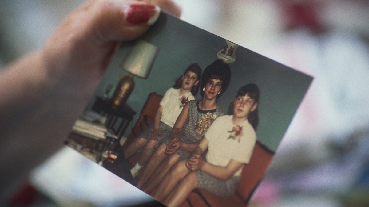 Jean holding a childhood family photo of her, Pat Carroll, and Dorothy Carroll sitting on the couch.