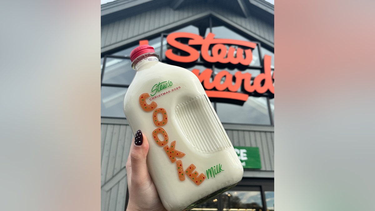 Stew Leonard's Cookie Milk glass jar held up in front of a Stew Leonard's grocery store.