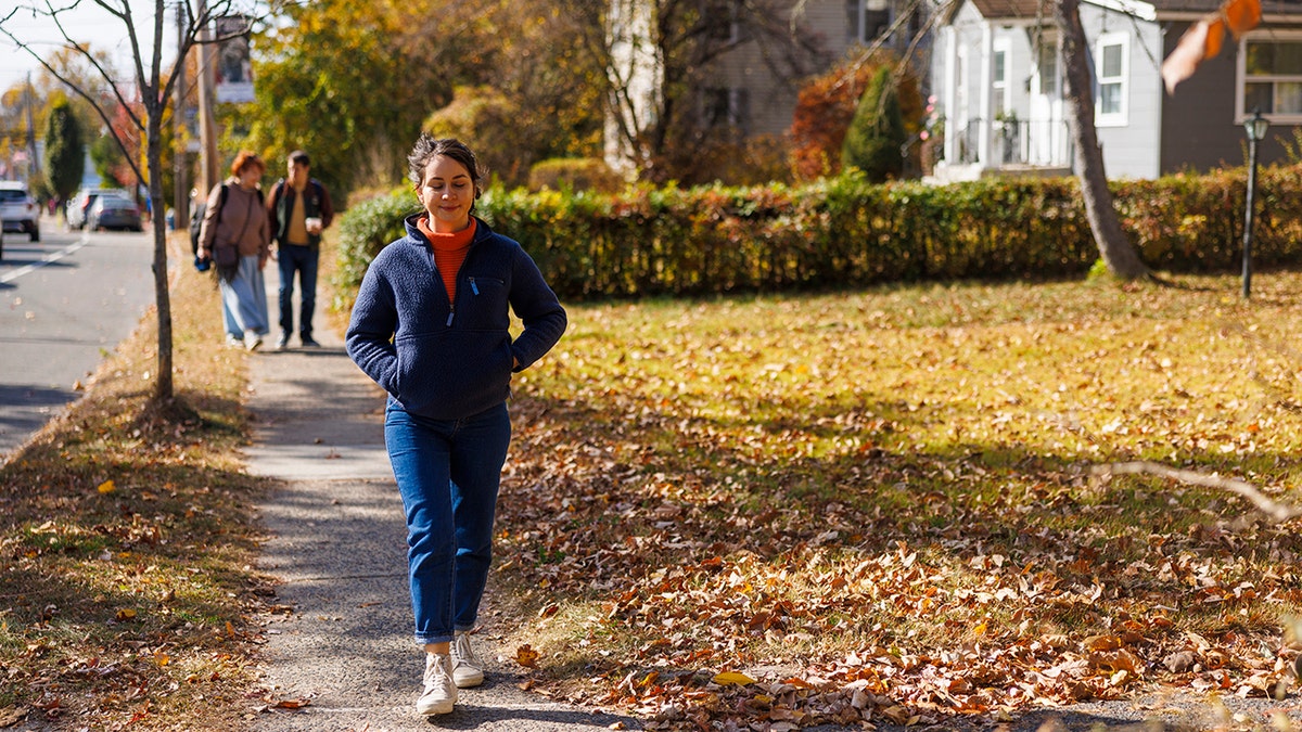 Young woman happily walking down suburban street during fall.