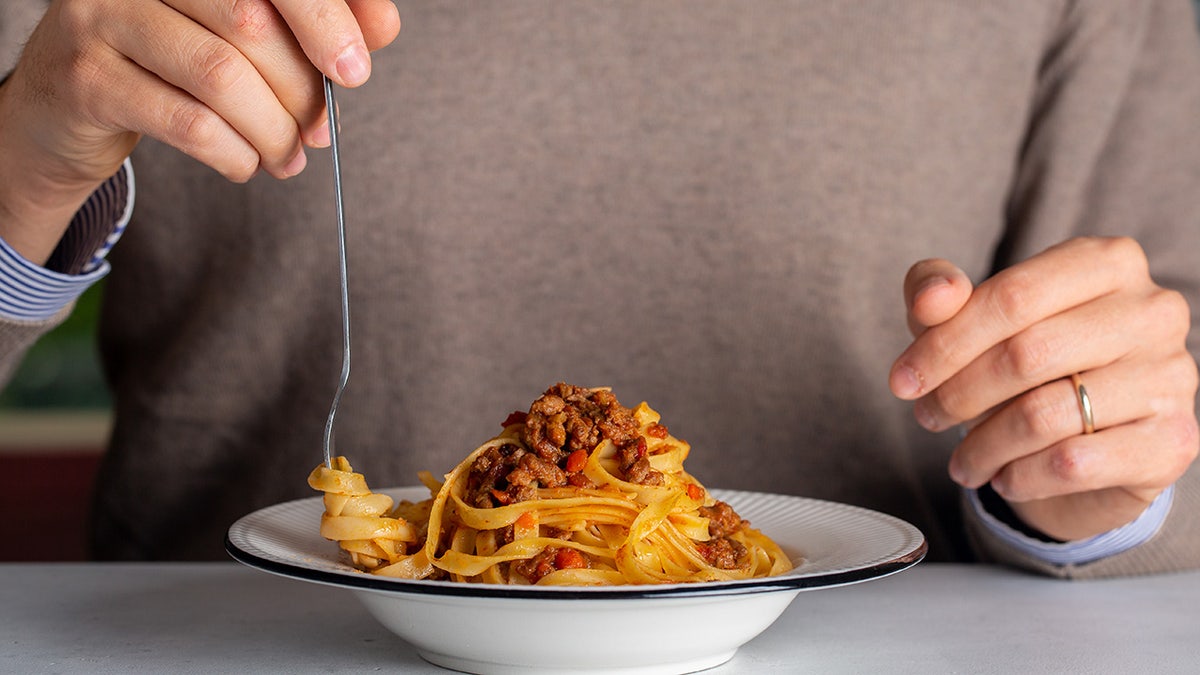 A man eating pasta and meat sauce, hands and bowl seen up close as he twirls pasta around fork.