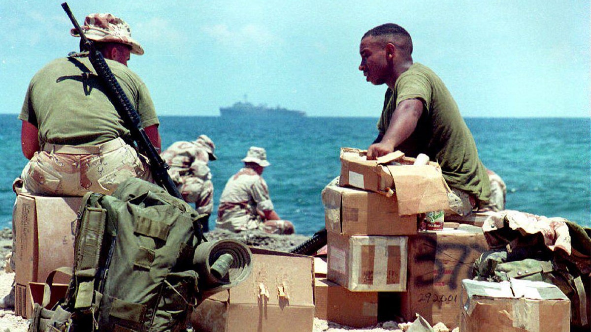 U.S. soldiers wait with their belongings to embark on a U.S. Navy ship, which appears in the background, 23 March 1995 at Mogadishu harbor. The last U.S. soldiers are scheduled to leave Somalia 25 March 1995.