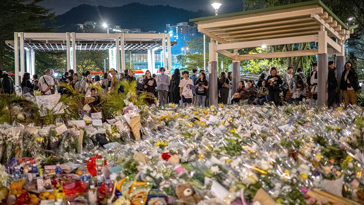 Los dolientes se reúnen frente a un complejo de viviendas en Hong Kong para depositar flores en memoria de los muertos en el incendio.