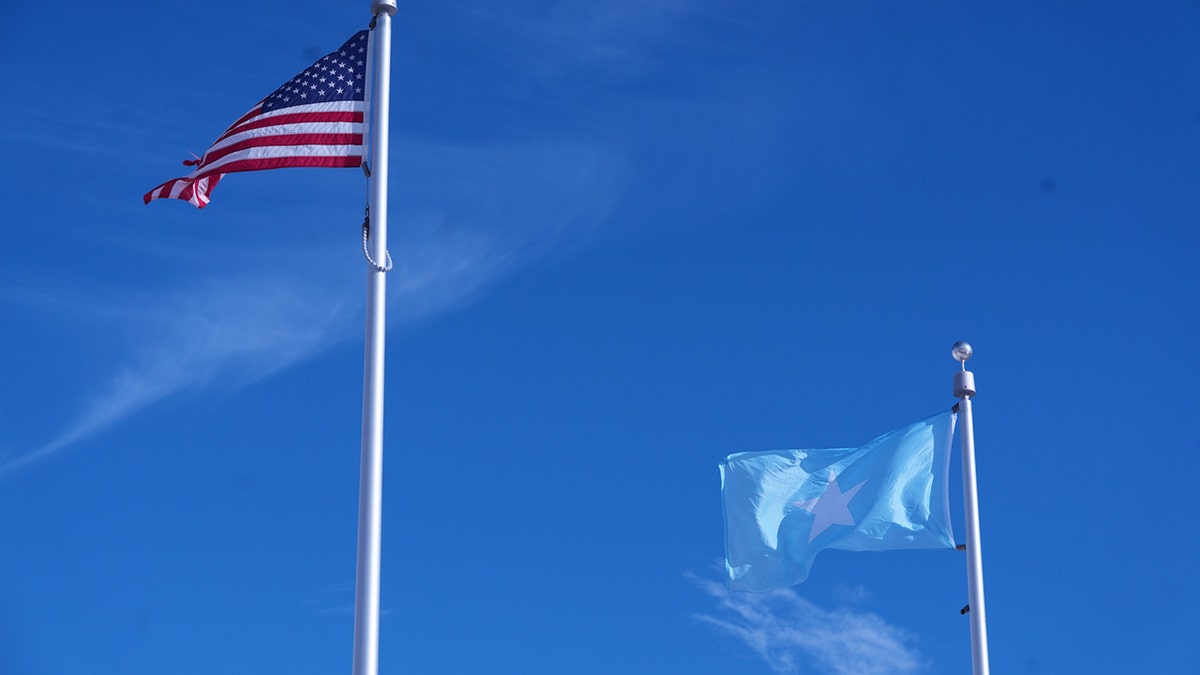 Somali flag flies beneath American flag with clear blue sky background