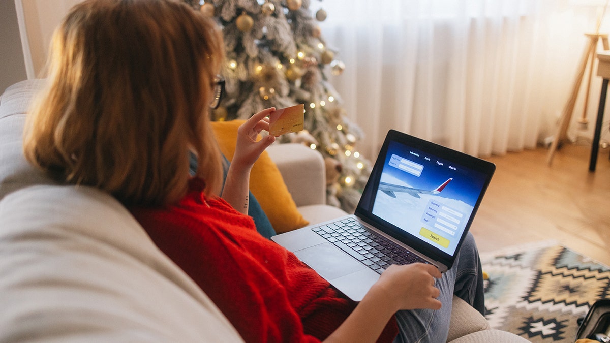 A woman is looking at a credit card while she has her laptop open to an airline booking website.