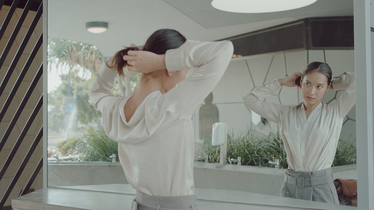 Person styling their hair in front of a large mirror in a modern indoor space.