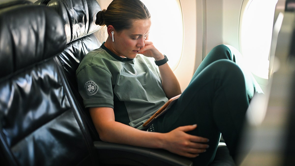 Airline passenger sitting comfortably in a window seat using a tablet during a flight.
