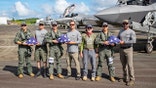 Men hold folded American flags on an airstrip beside military aircrafts.