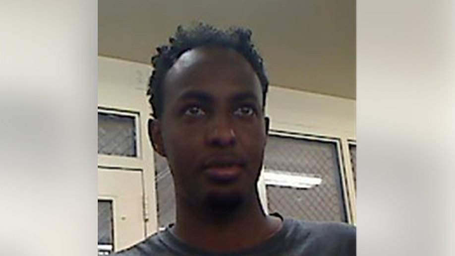 Man looks slightly upward in an indoor room with wire-mesh windows behind him.
