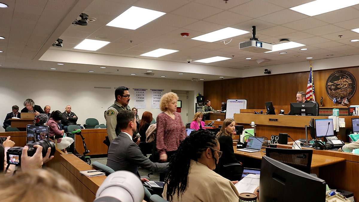 Ashlee Buzzard walks through a Lompoc courtroom escorted by law enforcement as court staff and observers look on.