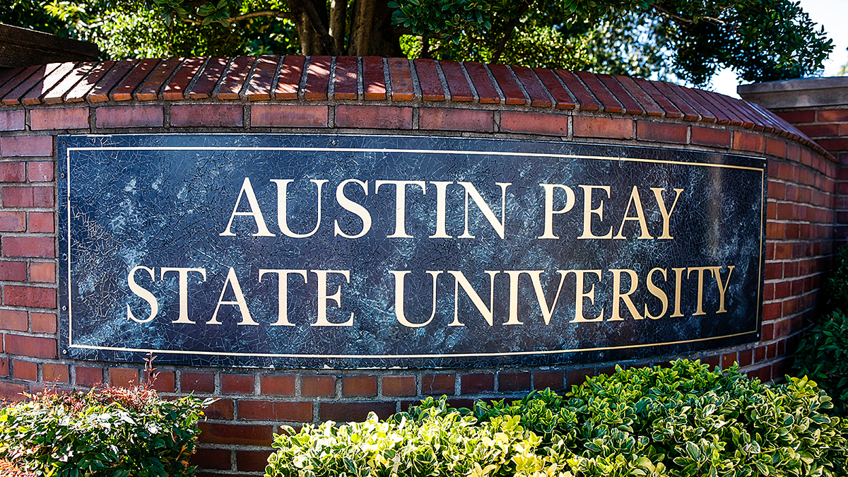 Austin Peay State University Entrance Sign fixed to a red brick wall surrounded by trees and small hedge shrubs