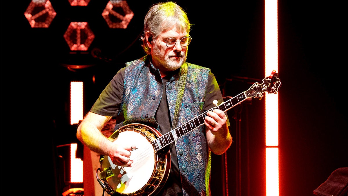 Béla Fleck performs onstage with a banjo during a live concert.