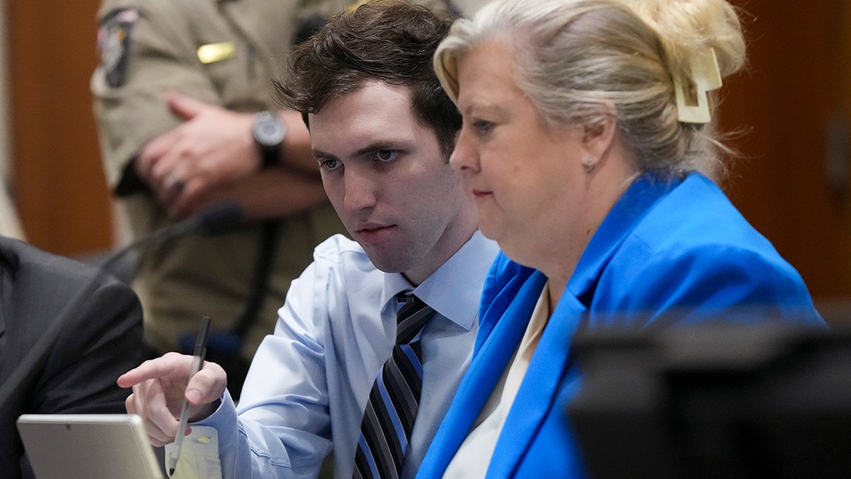 Tyler Robinson pointing while seated next to defense attorney Kathryn Nester in court