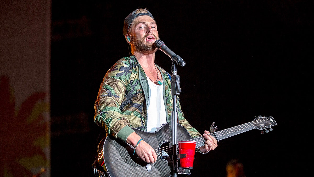 Chris Lane performs onstage with a microphone at an outdoor amphitheater concert.