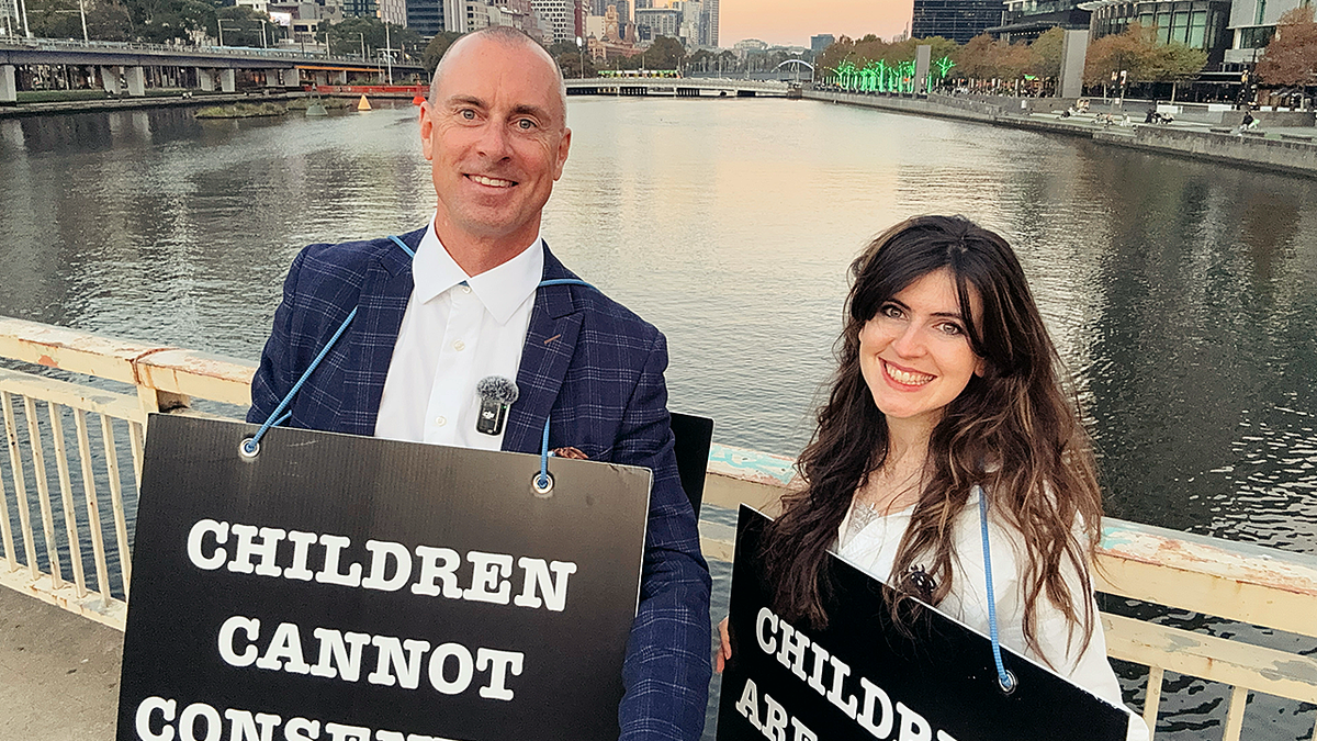 Chris Elston and Lois McLatchie Miller smiling while holding signs