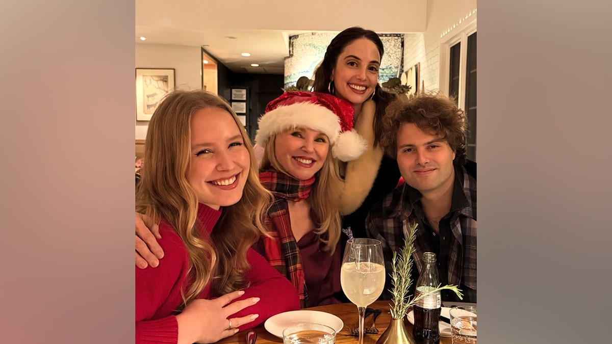 Christie Brinkley smiles while celebrating Christmas Eve with her children Sailor Brinkley Cook, Alexa Ray Joel and Jack Brinkley Cook at a dinner table.
