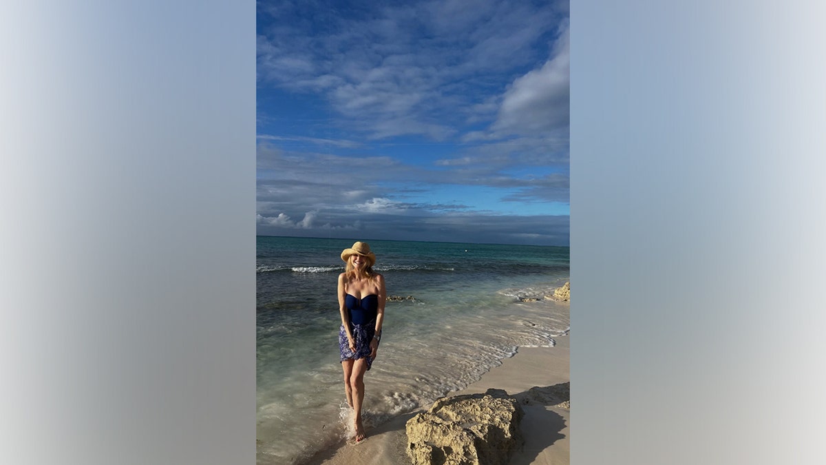 Christie Brinkley walks barefoot along the shoreline during a tropical vacation as waves wash in around her feet.